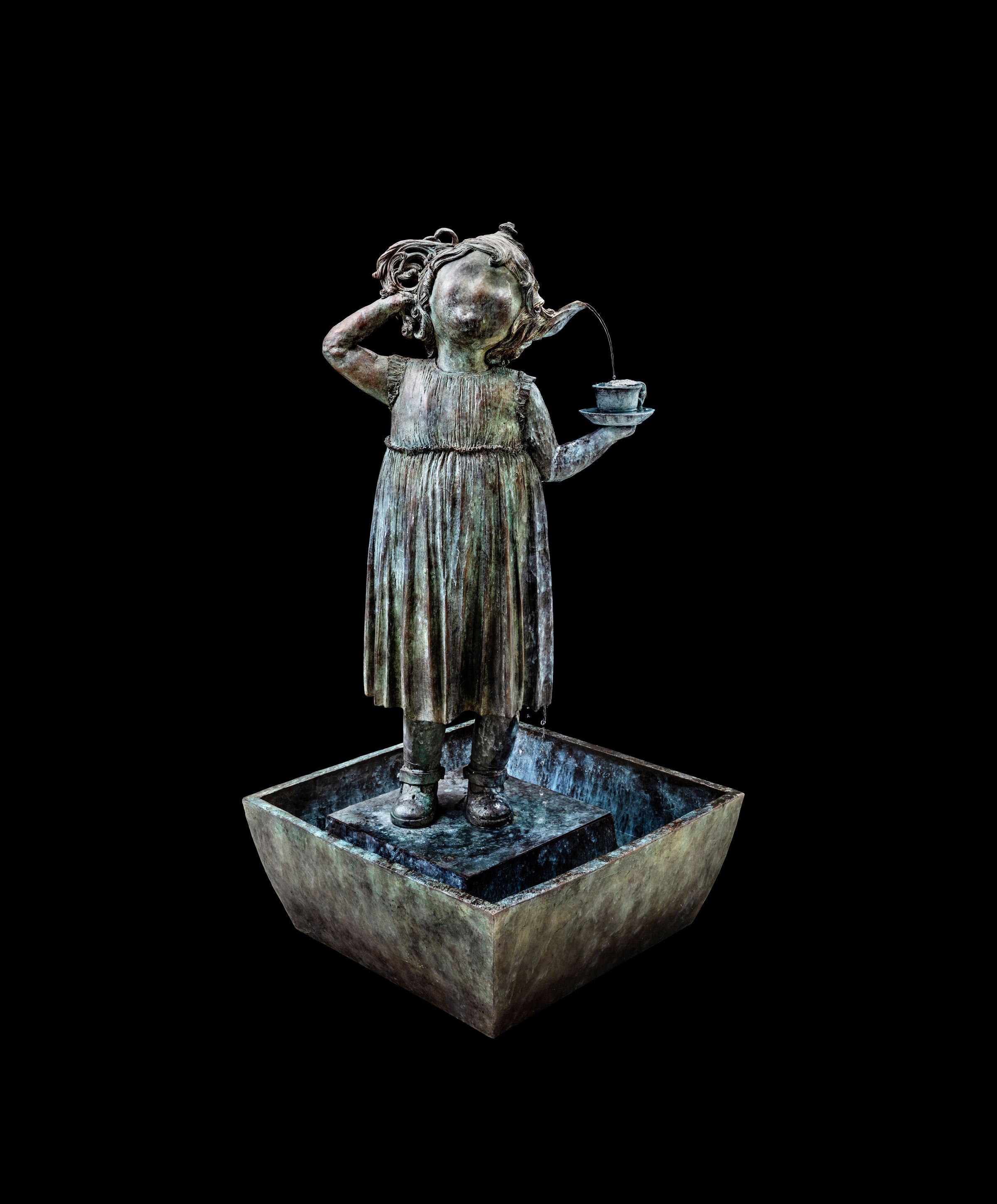 Bronzeskulptur af pige med opsat hår i kjole, stående i en fontæne med vandstråle, der løber fra øret til en kop i hånden. Maria Rubinke, I Come From a Place, I Long to Return To, 2019. Højde: 140 cm. Unika.